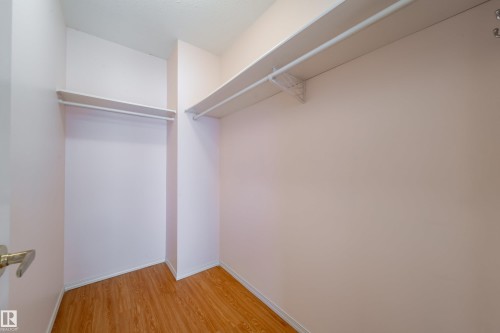 Walk-in closet featuring wood-finish flooring, white walls, and built-in shelving with hanging rods - 120 13320 124 Street Nw, Edmonton, AB 