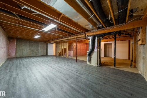 Spacious unfinished basement featuring gray wood-finish flooring, exposed ceiling joists, and concrete walls - 120 13320 124 Street Nw, Edmonton, AB 