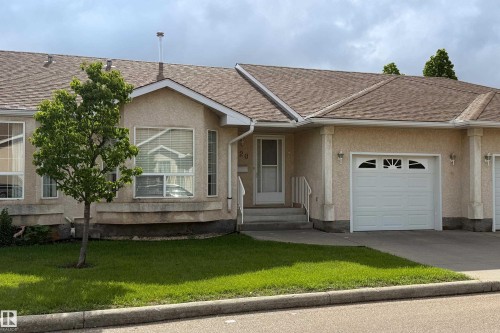 Cream-colored stucco exterior featuring an attached garage with a decorative arched window insert - 120 13320 124 Street Nw, Edmonton, AB 
