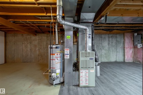 Basement space featuring concrete walls, exposed ceiling joists, utility equipment including a water heater and furnace, and a section of wood-finish flooring - 120 13320 124 Street Nw, Edmonton, AB 