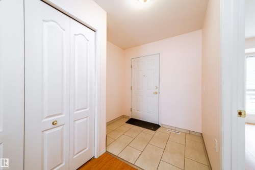 Entryway featuring a white paneled door, light-toned tile flooring, and a bifold closet with brass hardware - 120 13320 124 Street Nw, Edmonton, AB 