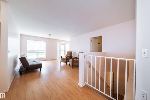 Spacious interior featuring wood-finish flooring, white painted walls, and a prominent staircase with white railings - 120 13320 124 Street Nw, Edmonton, AB 