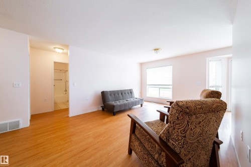 Spacious interior with wood-finish flooring, white walls, and a large window providing ample natural light - 120 13320 124 Street Nw, Edmonton, AB 