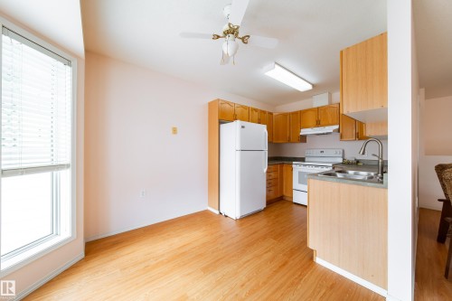 Kitchen and dining area featuring wood-finish flooring, white appliances, and light wood cabinetry - 120 13320 124 Street Nw, Edmonton, AB 