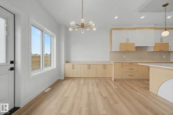 Open-concept living area featuring wood-finish flooring, a contemporary brass chandelier, a large window, a kitchen island, and two-tone cabinetry with light countertops - 