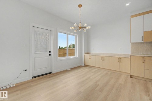 Open-concept space featuring light wood-finish flooring, a contemporary chandelier, built-in cabinetry with a light countertop, and a white door with a clear glass insert - 2 Willow Heights Drive, Stony Plain, AB 