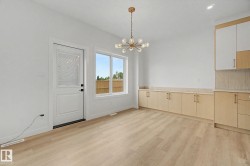 Open-concept space featuring light wood-finish flooring, a contemporary chandelier, built-in cabinetry with a light countertop, and a white door with a clear glass insert - 