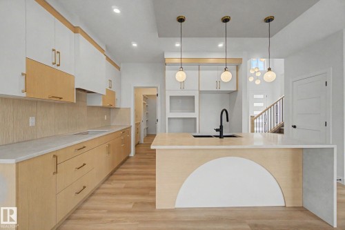 Contemporary kitchen featuring a large island with integrated sink, three suspended globe pendant lights, and contrasting two-tone cabinetry - 2 Willow Heights Drive, Stony Plain, AB 