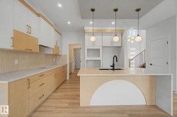 Contemporary kitchen featuring a large island with integrated sink, three suspended globe pendant lights, and contrasting two-tone cabinetry - 