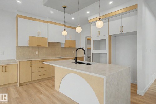 Open-concept kitchen featuring two-tone cabinetry with gold hardware, a central island with a black faucet and integrated sink, recessed lighting, and wood-finish flooring - 2 Willow Heights Drive, Stony Plain, AB 
