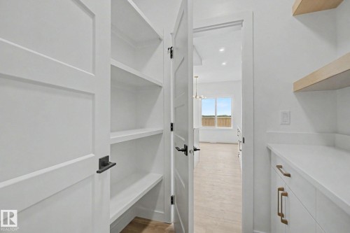Walk-in pantry featuring built-in shelving, white shaker-style cabinetry, matte black hardware, and light wood-finish flooring - 2 Willow Heights Drive, Stony Plain, AB 