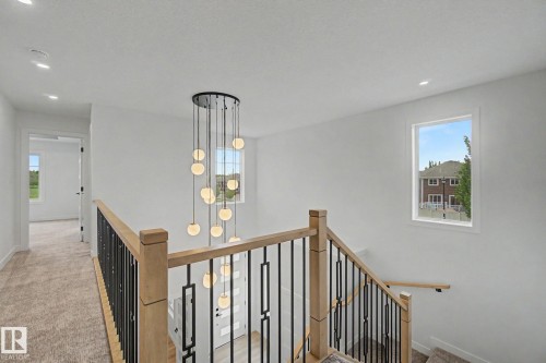 Modern multi-level chandelier illuminating a staircase with wood newel posts and black metal balusters - 2 Willow Heights Drive, Stony Plain, AB 