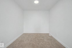 Recessed ceiling light illuminating a room with neutral-toned carpeting, white walls, and white baseboards - 