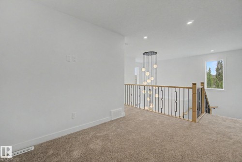 Open concept area featuring a modern multi-pendant chandelier, light wood-finish and black metal railings, plush carpeted flooring, a recessed window, and white trim - 2 Willow Heights Drive, Stony Plain, AB 