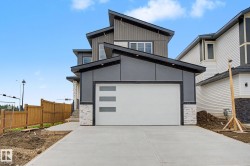 Modern exterior featuring a prominent garage with decorative windows, sloped rooflines, gray siding, white horizontal siding, and stone accents - 