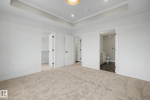 Spacious carpeted room featuring a tray ceiling with recessed lighting, white five-panel interior doors, and a neutral color palette - 2 Willow Heights Drive, Stony Plain, AB 