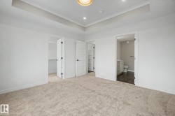 Spacious carpeted room featuring a tray ceiling with recessed lighting, white five-panel interior doors, and a neutral color palette - 