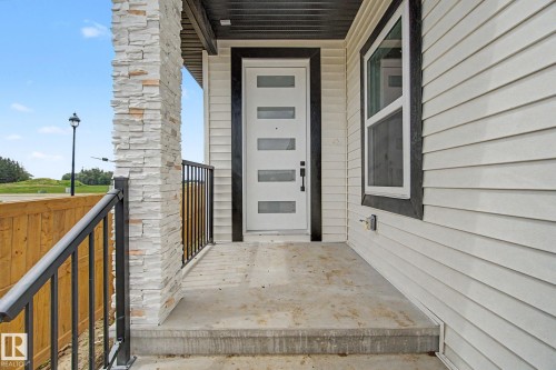 Front entry featuring a modern white door with horizontal glass inserts, flanked by a stone-clad pillar and a black metal railing - 2 Willow Heights Drive, Stony Plain, AB 