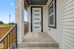 Front entry featuring a modern white door with horizontal glass inserts, flanked by a stone-clad pillar and a black metal railing - 