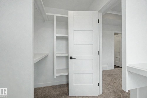 Walk-in closet featuring white built-in shelving, a hanging rod, and light-toned carpeting - 2 Willow Heights Drive, Stony Plain, AB 