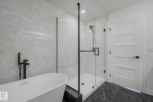 Contemporary bathroom featuring a freestanding soaking tub with a matte black floor-mounted faucet, a frameless glass shower enclosure, and dark stone-finish floor tiling - 2 Willow Heights Drive, Stony Plain, AB 