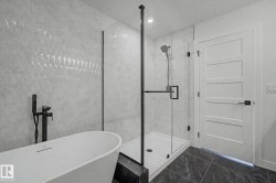 Contemporary bathroom featuring a freestanding soaking tub with a matte black floor-mounted faucet, a frameless glass shower enclosure, and dark stone-finish floor tiling - 