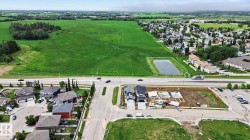 Aerial representation of a developing suburban area bordered by expansive green fields and a roadway - 