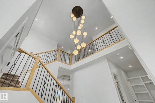 Two-story foyer featuring a contemporary chandelier, recessed lighting, wood-finish handrails, black metal balusters, and carpeted stairs - 2 Willow Heights Drive, Stony Plain, AB 
