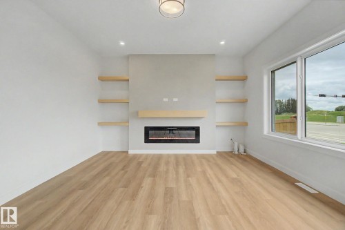 Living area featuring an electric fireplace with a light-toned mantel, flanking wood-finish floating shelves, wood-finish flooring, and a large window - 2 Willow Heights Drive, Stony Plain, AB 