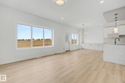 Open-concept living space featuring wood-finish flooring, white walls, and contemporary light fixtures - 