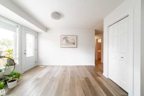 Bright entryway featuring light wood-finish flooring, a white paneled entry door with decorative glass, and a flush-mount ceiling light fixture - 5607 188A Street, Edmonton, AB 