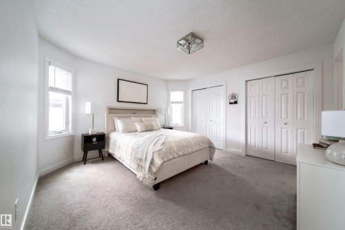 Carpeted room featuring multiple windows, two sets of bi-fold closet doors, and a ceiling-mounted light fixture - 5607 188A Street, Edmonton, AB 