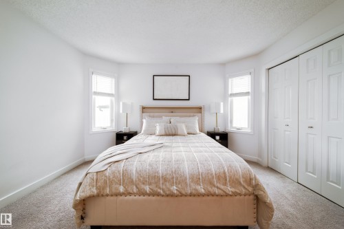 Bedroom featuring light gray carpet flooring, white painted walls, two windows with blinds, and white bi-fold closet doors - 5607 188A Street, Edmonton, AB 
