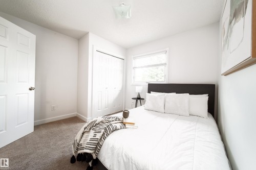 Bright bedroom featuring neutral carpet flooring, a white paneled door, and a window with blinds - 5607 188A Street, Edmonton, AB 