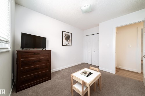 Carpeted room with white walls, featuring a window with horizontal blinds, a ceiling-mounted light fixture, and bifold closet doors - 5607 188A Street, Edmonton, AB 