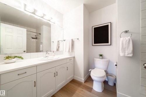 Bathroom featuring a white vanity with extensive counter space and undermount sink, a large wall-mounted mirror, a four-light vanity fixture, wood-finish flooring, and a white toilet - 5607 188A Street, Edmonton, AB 