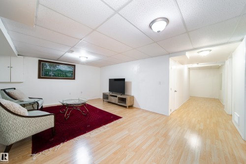 Spacious lower-level area featuring wood-finish flooring, white walls, and a suspended ceiling with flush-mount lighting - 5607 188A Street, Edmonton, AB 