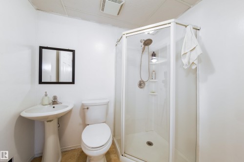 Compact bathroom featuring a glass-enclosed shower, pedestal sink, and toilet - 5607 188A Street, Edmonton, AB 