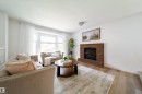 Bright living space featuring a brick fireplace with hearth, wood-finish flooring, and a bay window with ample natural light - 5607 188A Street, Edmonton, AB 