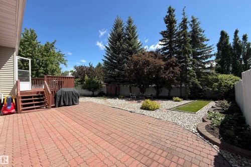 Expansive outdoor living area featuring a red paver patio, wood deck with stairs, gravel landscaping, established trees, and a dedicated bocce ball court - 5607 188A Street, Edmonton, AB 