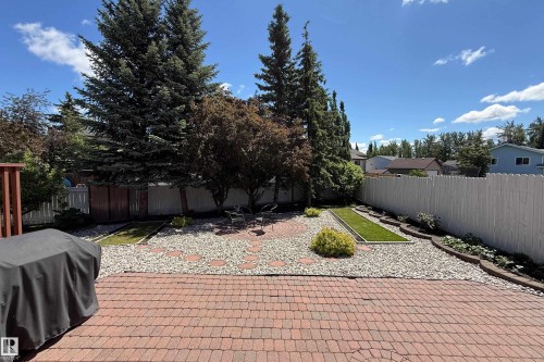 Brick paver patio extending to a landscaped backyard featuring decorative gravel, circular paver accents, planting beds, and mature trees - 5607 188A Street, Edmonton, AB 