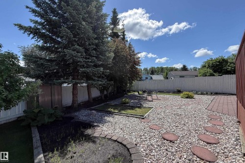 Expansive backyard featuring a large stone patio, a red paver pathway, and multiple garden beds - 5607 188A Street, Edmonton, AB 