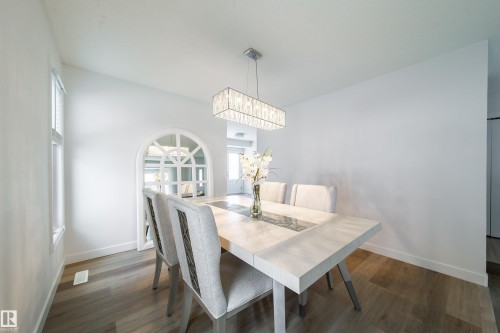 Dining space featuring wood-finish flooring, a rectangular chandelier, white painted walls, and an arched interior window with a decorative grid - 5607 188A Street, Edmonton, AB 