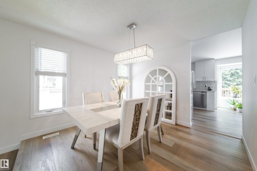 Bright dining area featuring wood-finish flooring, a contemporary rectangular chandelier, and a decorative arched wall niche - 5607 188A Street, Edmonton, AB 