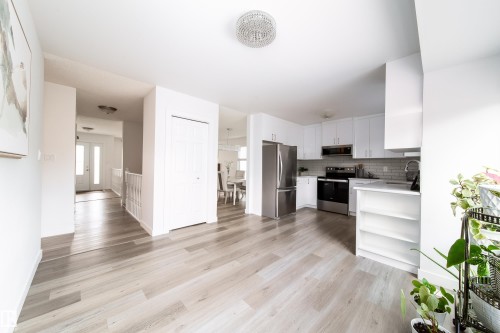Open-concept living area featuring light wood-finish flooring, a modern white kitchen with stainless steel appliances, white cabinetry, a subway tile backsplash, and recessed and pendant lighting - 5607 188A Street, Edmonton, AB 