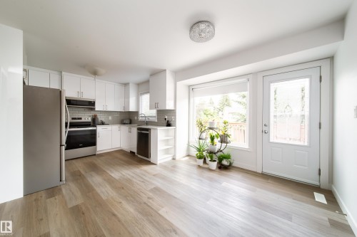 Open-concept kitchen and dining area featuring wood-finish flooring, white cabinetry, and stainless steel appliances - 5607 188A Street, Edmonton, AB 