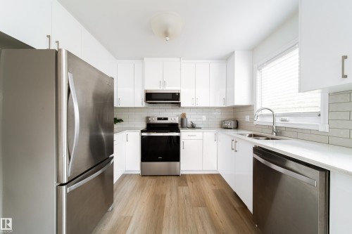 Kitchen featuring white cabinetry, stainless steel appliances, wood-finish flooring, light-toned countertops, and a subway tile backsplash - 5607 188A Street, Edmonton, AB 
