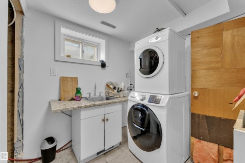 Dedicated laundry area featuring a stacked washer and dryer, utility sink with a granite-finish countertop, and white cabinetry - 9606 161 Street, Edmonton, AB 