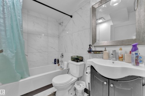 Bathroom featuring large format marble-look wall tiling, a white bathtub with chrome fixtures, and a dark wood-finish vanity with an integrated sink - 9606 161 Street, Edmonton, AB 