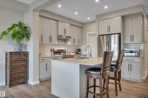 Modern kitchen featuring light gray cabinetry, stainless steel appliances, a white subway tile backsplash, recessed lighting, and wood-finish flooring - 157 Larch Crescent, Leduc, AB 